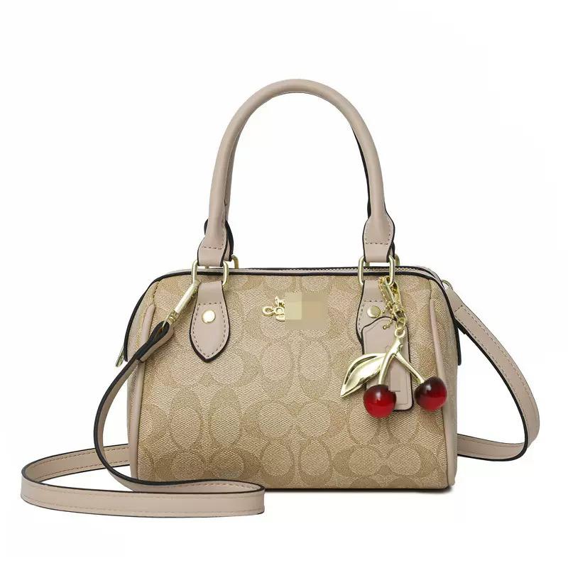Beige signature print mini handbag with top handles, detachable strap, gold hardware, and cherry charm accessory.