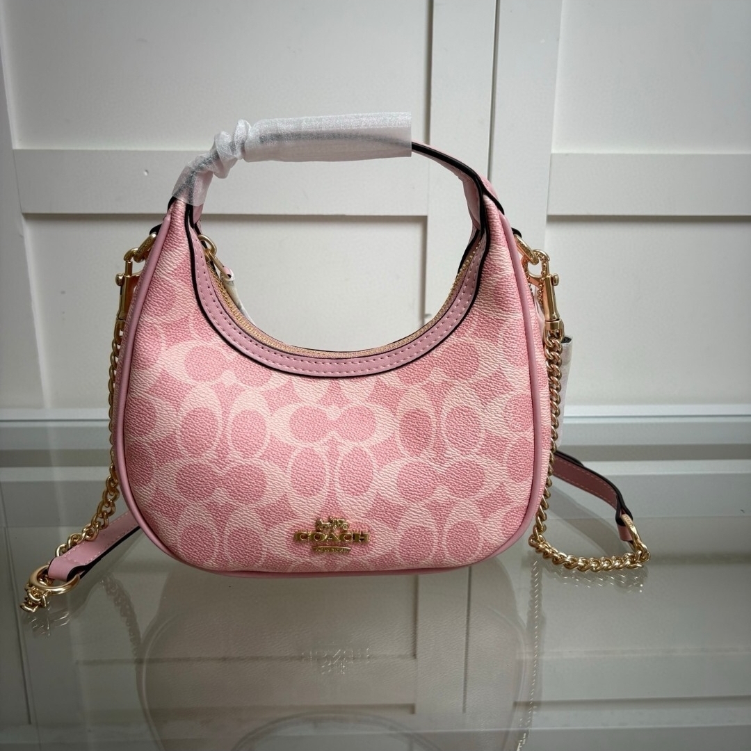 Pink mini shoulder bag with signature pattern, gold chain strap, and top handle, displayed on a reflective surface.